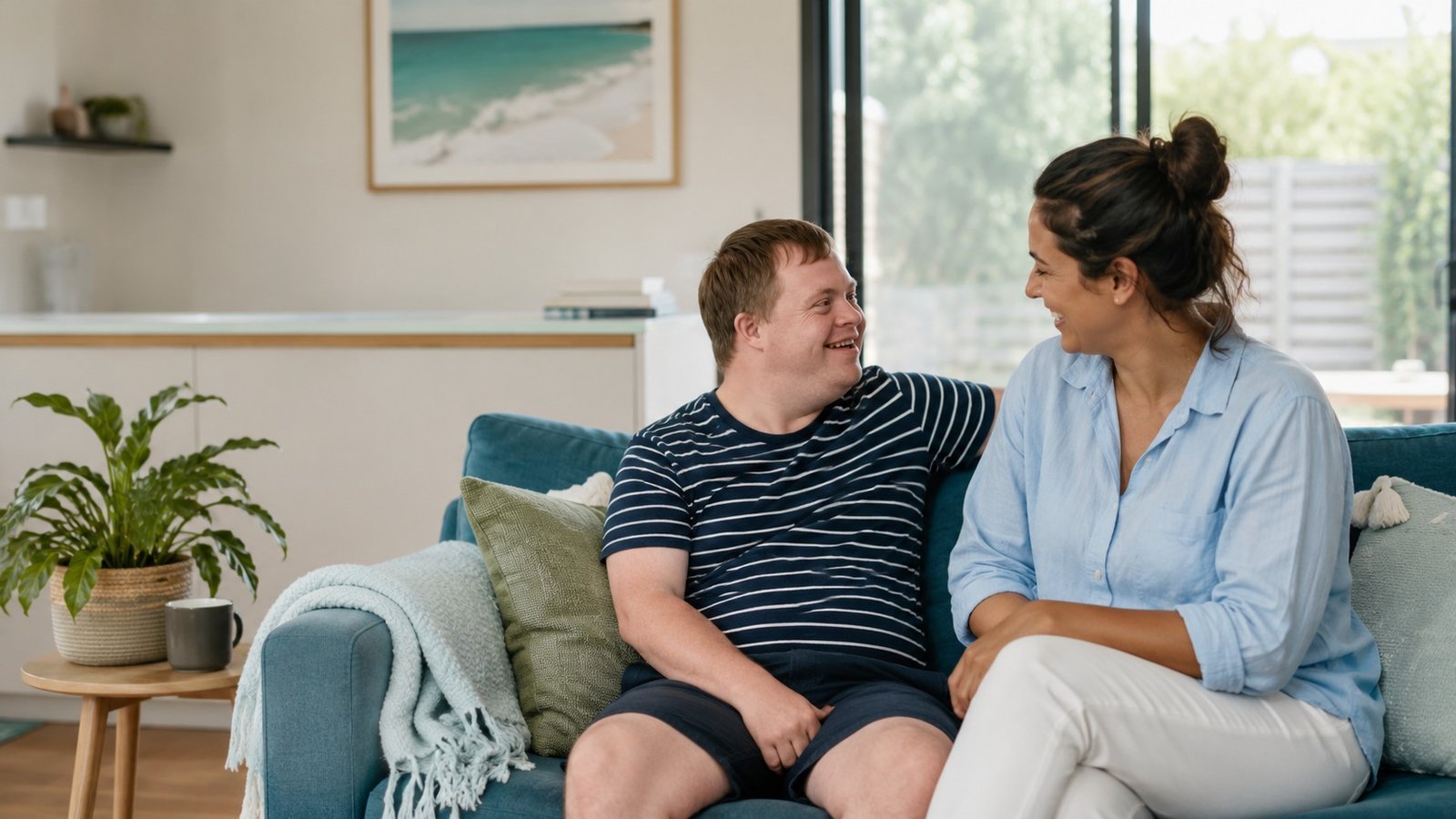 A relaxed one-to-one moment between a support worker and a participant chatting on a couch at home